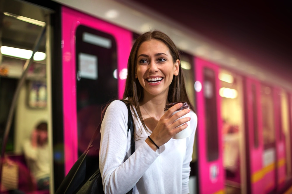 Lächelnde Frau mit Kaffeebecher in der Hand steigt aus einer Straßenbahn aus.
