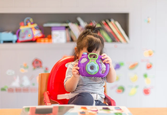 Arbeitgeberzuschuss zur Kinderbetreuung – steuerfreier Benefit für berufstätige Eltern Ein Kind im Kindergarten spielt mit einer Spielzeug-Kamera