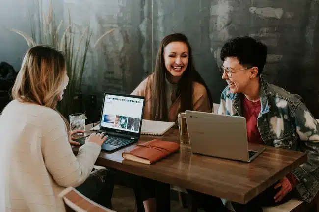 Arbeitskollegen die lachend zusammen an einem Tisch sitzen - Repräsentation von corporate benefits